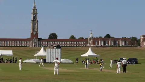 George Franks Photographer Young cricketers playing a match on a cricket pitch at The Royal Hospital School. The school building is in the background of the image.