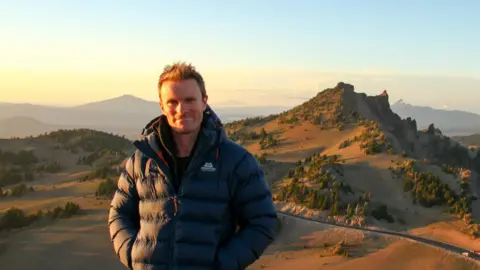 Supplied James Adler pictured in a black jacket in front of hills.