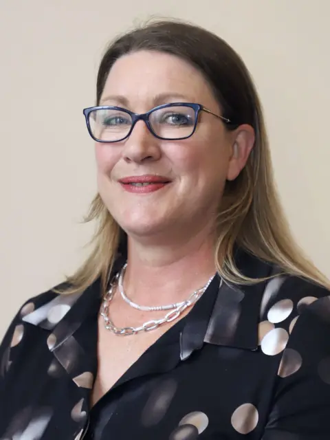 Dumfries and Galloway Council Gail Macgregor with long brownish/blonde hair and glasses in a dark top with coloured spots on it wearing two silver necklaces