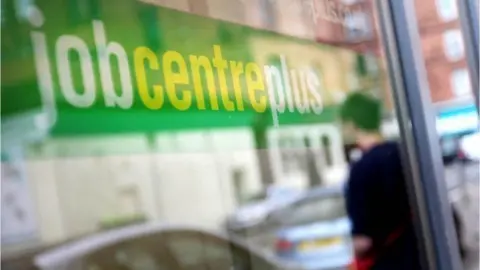 PA Media Close up of a Job Centre Plus window shoeing the reflection of a woman with her back to the office