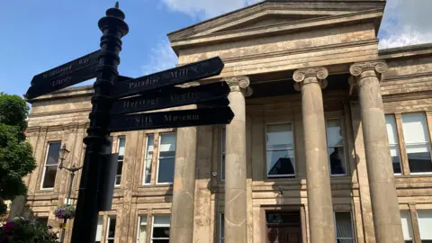 Macclesfield Town Hall with a sign post pointing to various locations in front of it, including the Silk Museum