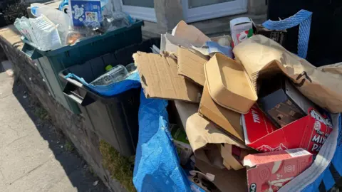Overflowing boxes of recycling and rubbish, sitting out on a pavement