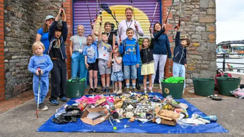 Great Western Railway A group of five adults and eight children pose in front of a blue tarpaulin covered in trash