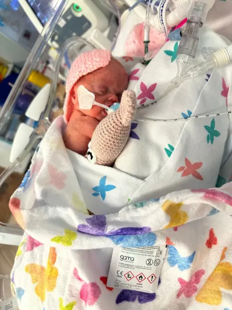 Caitlin Duncan A baby on a colourful cot with medical tubes all around