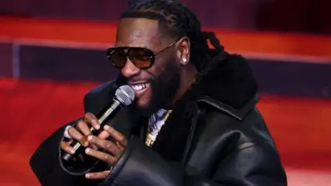 Nigerian music star Burna Boy performs wearing a black jacket and holding a microphone