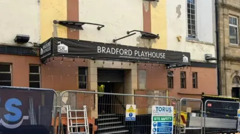 The outside of a building with scaffolding work being carried out. There is a black banner above the entrance that reads Bradford Playhouse