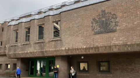 Chelmsford Crown Court pictured on a grey day. It is a dull building made of brick and has green entrance doors.