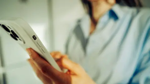 An anonymous person holds a white smartphone with two hands, they're wearing a blue shirt.