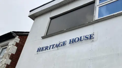 A white building with blue lettering to say 'Heritage House'