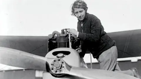 Black and white photo dated 10/1/30 of Amy Johnson on top of a plane at the London Aeroplane Club