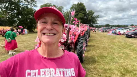 Mousumi Bakshi/BBC A woman stands in front of tractor decorated in pink flowers. She is wearing a pink T-shirt and cap. 