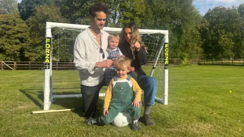 Family photo The family kneel in a park in front of a small football goal with Lucky sat on a football and baby Dusty on his dad's knee