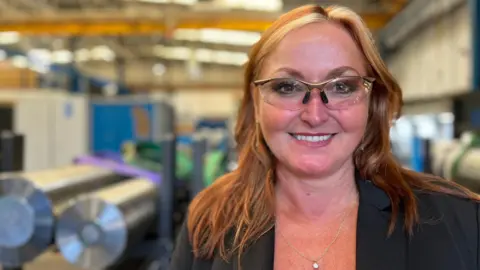 Charlotte Rose/BBC Andrea Wilson wears safety glasses on the shop floor of a factory with machines in the background