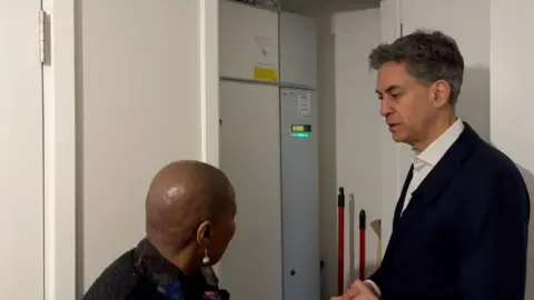 Ed Milliband looks at the heat pump installed in a recently built flat in Reading with the tennant living there.