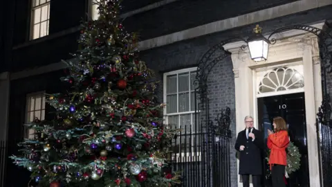 Downing Street Christmas tree, adorned with lights and decorations, stood outside number 10 alongside Sir Keir Starmer and his wife