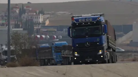 A convoy of blue lorries driving uphill on a slight bend 