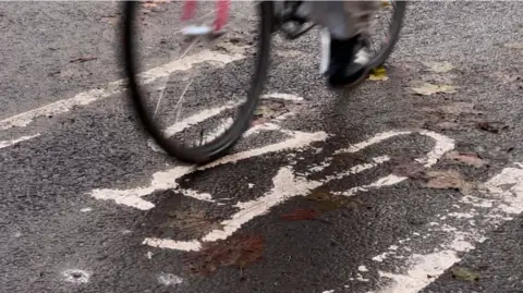 A close up of a cycle path in Oxford, with two wheels of a bike travelling over it.