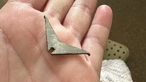 A hand holding a metallic spike which look like a boomerang with sharper edges.