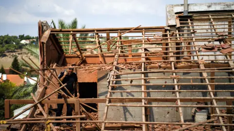 Reuters An Israeli policeman walks on the roof of a house in northern Israel that was hit by a rocket fired from Lebanon by Hezbollah (23 September 2024)