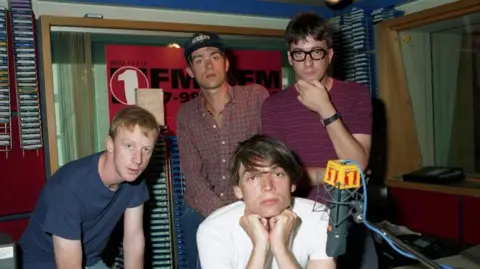 Four men stood next to each other. There is a radio microphone placed in front of them.