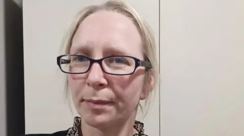 Handout Karen has taken a selfie. She has blond hair and is wearing glasses. She is standing in front of a white wall. 