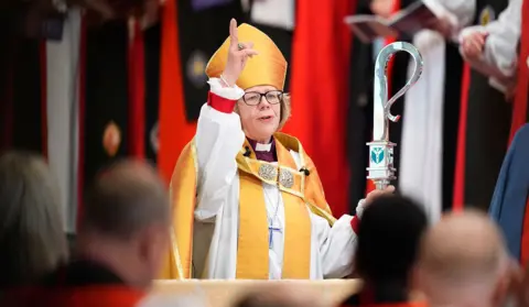 Jordan Pettitt / PA Media Dame Sarah raises a hand while holding staff and wearing robes in a close up photo of her giving a sermon during the ceremony.