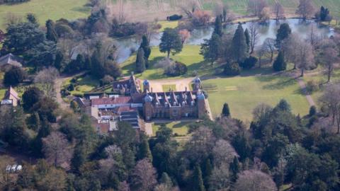 Aerial shot of stately home building surrounded by trees and parkland