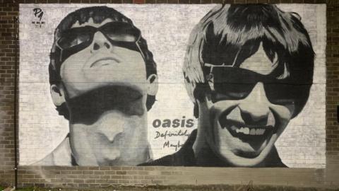 A large black and white mural featuring Noel Gallagher looking up and Liam Gallagher smiling, with the words 'Oasis Definitely Maybe' and Pic.One.Art's tag