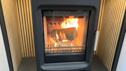 A log is burning inside a black stove. It is placed in an alcove in a shop's showroom.