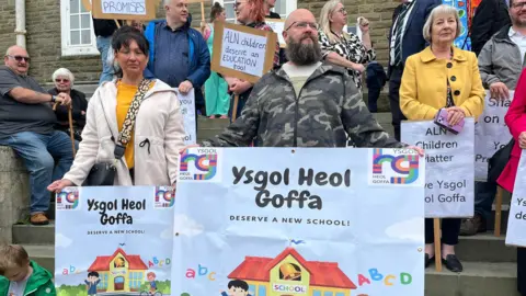 Parents on the steps of Carmarthenshire County Hall hold protest banners that read 'Ysgol Heol Goffa deserve a new school'