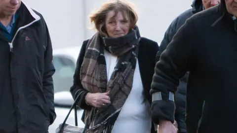 Athena Picture Agency Bridget Curtis who has fair hair and is wearing a white top, black jacket and black-and-brown scarf.