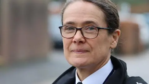 A head shot of Rachel Kearton, who has dark greying hair pulled back from her face and is wearing dark rimmed glasses. She is also wearing a navy police jacket over a white shirt and tie. 