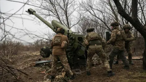 EPA Ukrainian soldiers in brown camouflage fire a howitzer into the distance