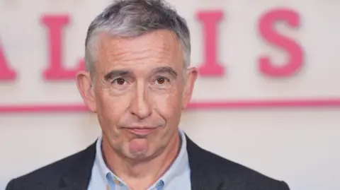 PA Media Steve Coogan with greying hair, clean shaven wearing a white Oxford-style shirt and a charcoal grey jacket
