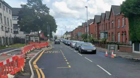 A street view of Tweedale Street. There are houses lining each side of the road, and traffic is backed up. There are roadworks being carried out on one side of the street.