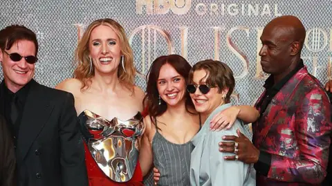 Getty Images Cast members posing at a premiere with arms over each other's shoulders and smiling and laughing