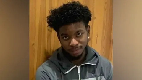 Met Police Robert Robinson smiles with his arms folded. He wears a grey zip-up hoodie. 