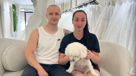 Lukasz Kurek, Agnieszka Uliasz and their dog Zara on a sofa in a wedding dress shop 