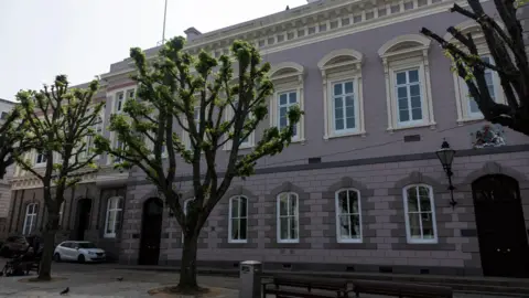 The States Building in St Helier, with trees and benches in the foreground on a sunny day.