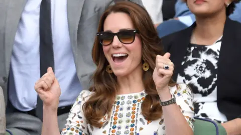 Getty Images The Princess of Wales with her hands up at Wimbledon in 2016. She is wearing a white printed dress, golden earrings and sunglasses.