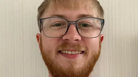 Conor Barton Conor Barton - a close up headshot. He has ginger hair and a short ginger beard and is wearing grey-rimmed glasses.