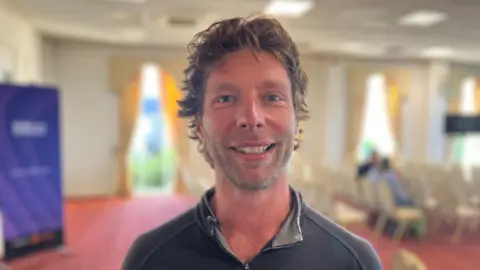 A man wearing a grey fleece, smiling at the camera