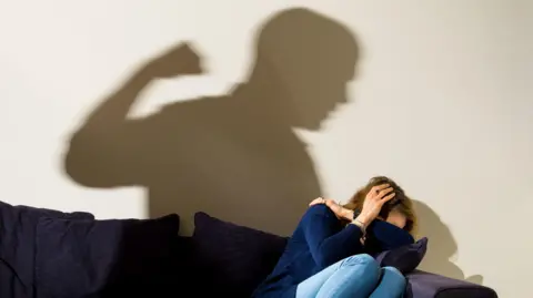 Dominic Lipinski/PA Wire Shadow of a man with a clenched fist as a woman cowers in the corner.