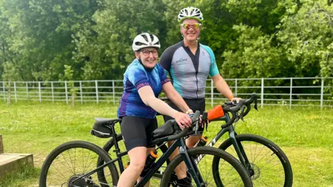 Collect/PA Real Life Sam and John smile at the camera, both with their bicycles wearing lycra