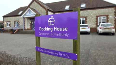 Paul Moseley/BBC A purple sign with white writing which says "Docking House, Care Home For The Elderly" is in the foreground with a care home building behind it.