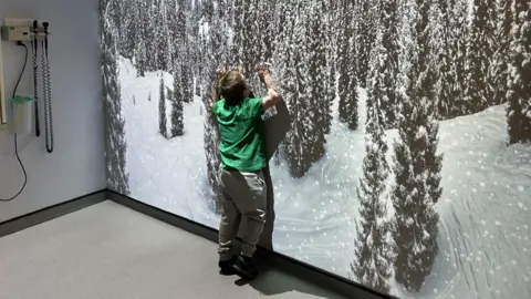 Ellis touching the lit up wall, which is in the snowy forest setting.