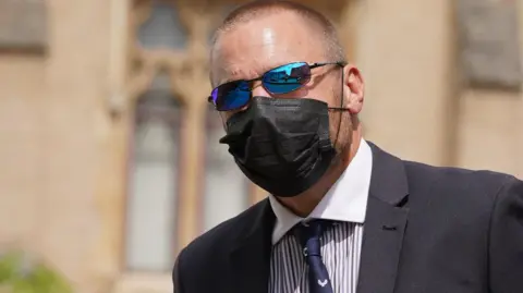 PA Media Craig Carter wearing a black face mask, blue tinted glasses and a navy jacket, striped shirt, navy tie walking into court on Friday 26 July