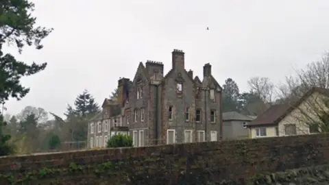 Google A fire-damaged stone building, seen over a stone wall 