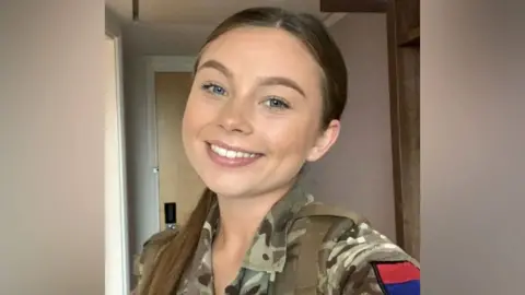 Gunner Jaysley Beck smiles in a selfie wearing a khaki camouflage jacket.