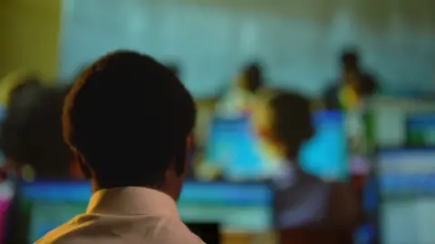 The rear view back of African learners' heads with the selective focus on a child looking at a computer screen. The people are all unrecognisable.